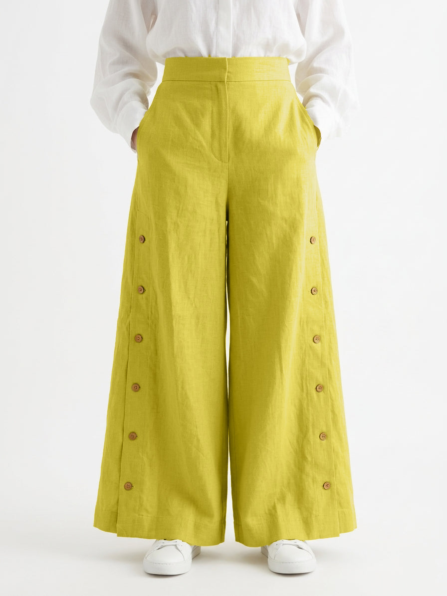 Yellow wide-leg pants with button details worn by a person on a white background