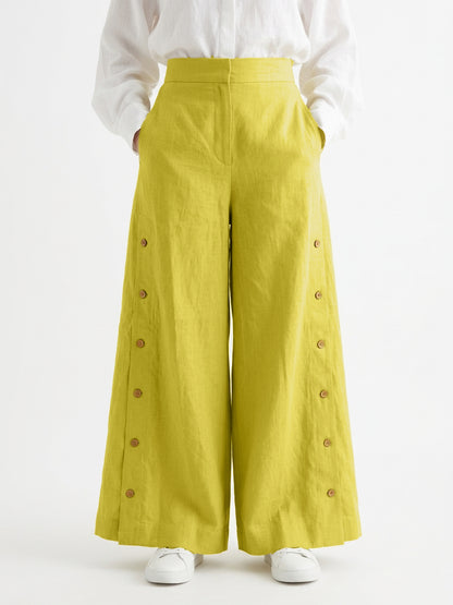Yellow wide-leg pants with button details worn by a person on a white background