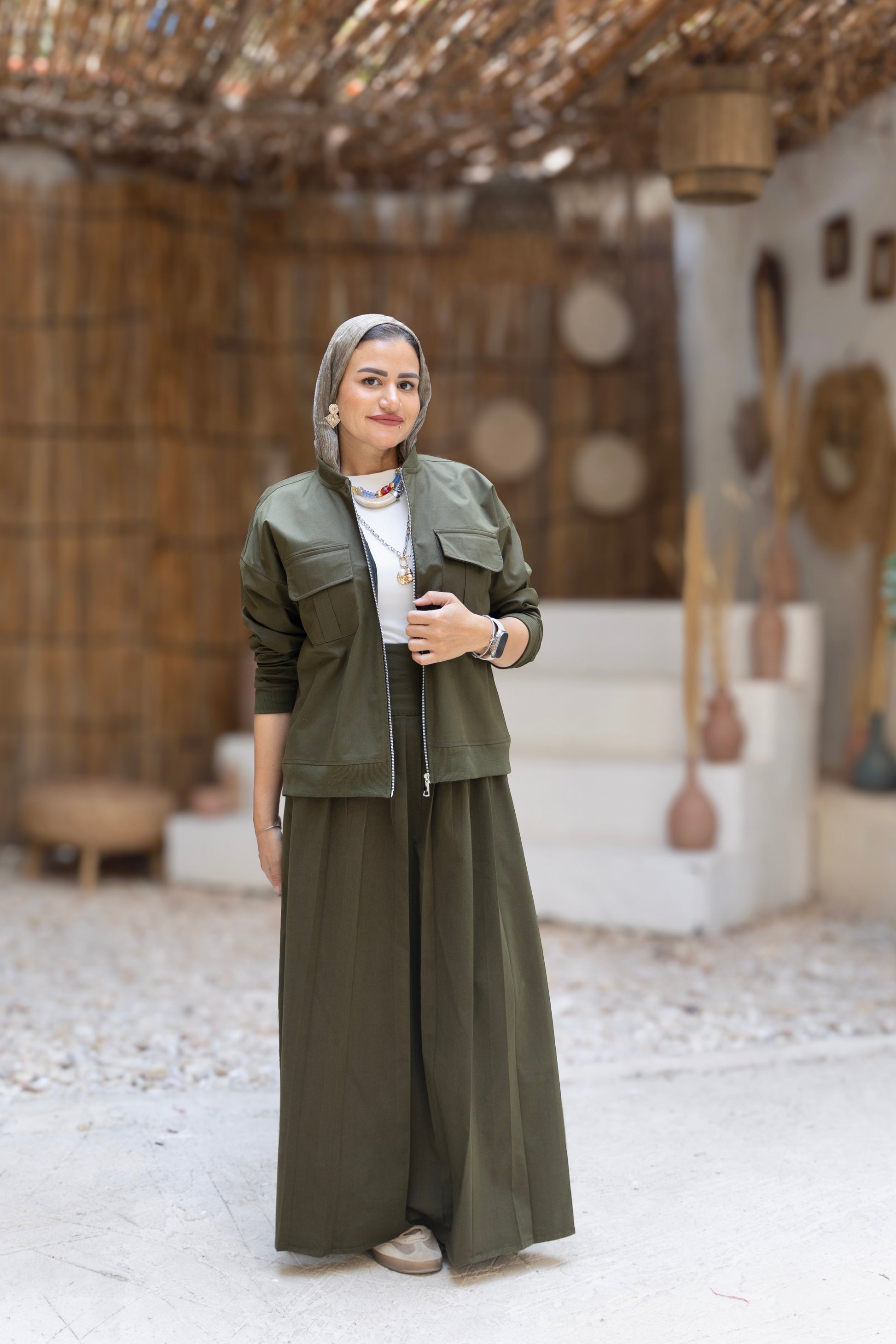 Woman in a green outfit standing in a rustic indoor setting with wooden walls and decor.
