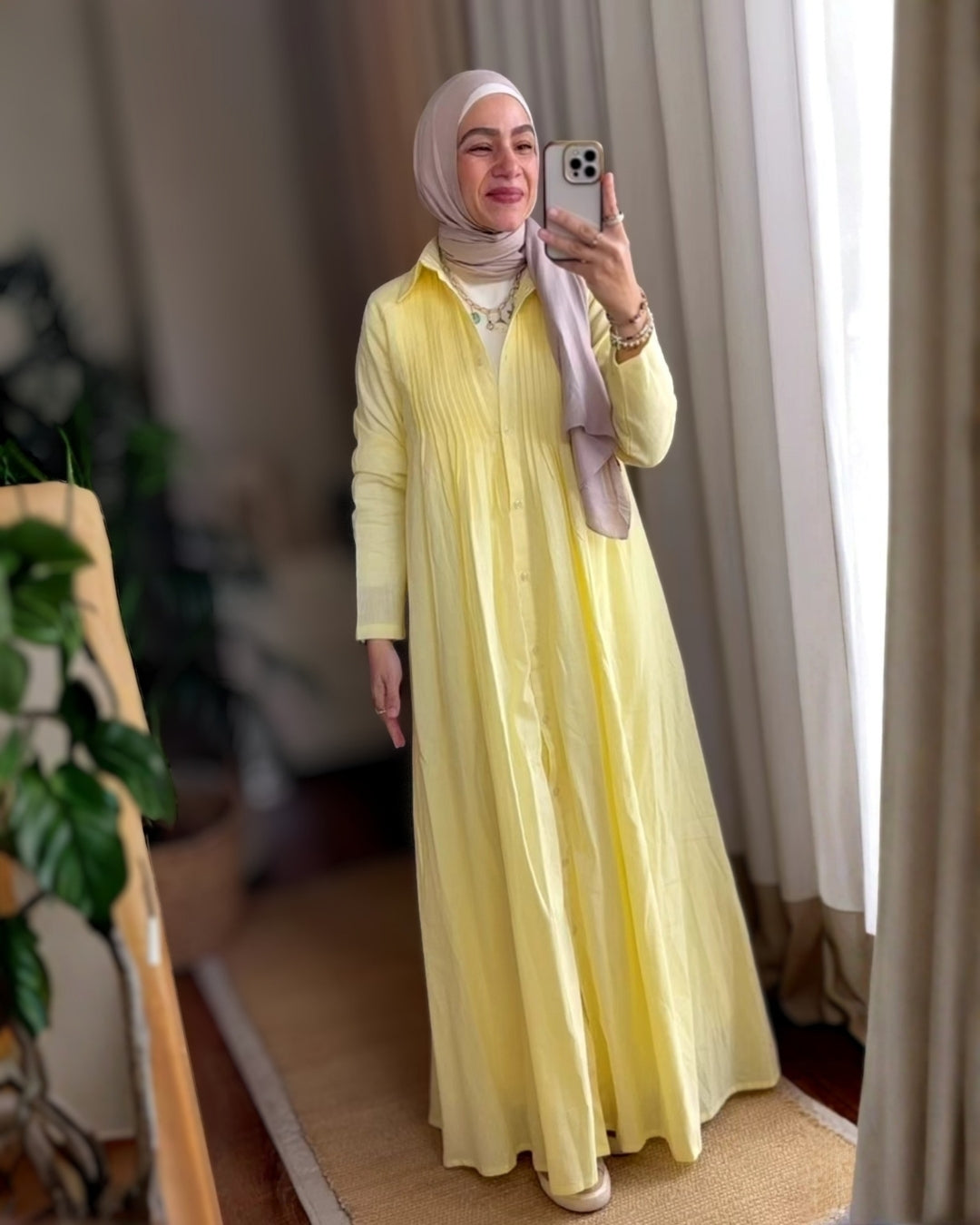 Woman wearing a yellow dress taking a mirror selfie indoors.