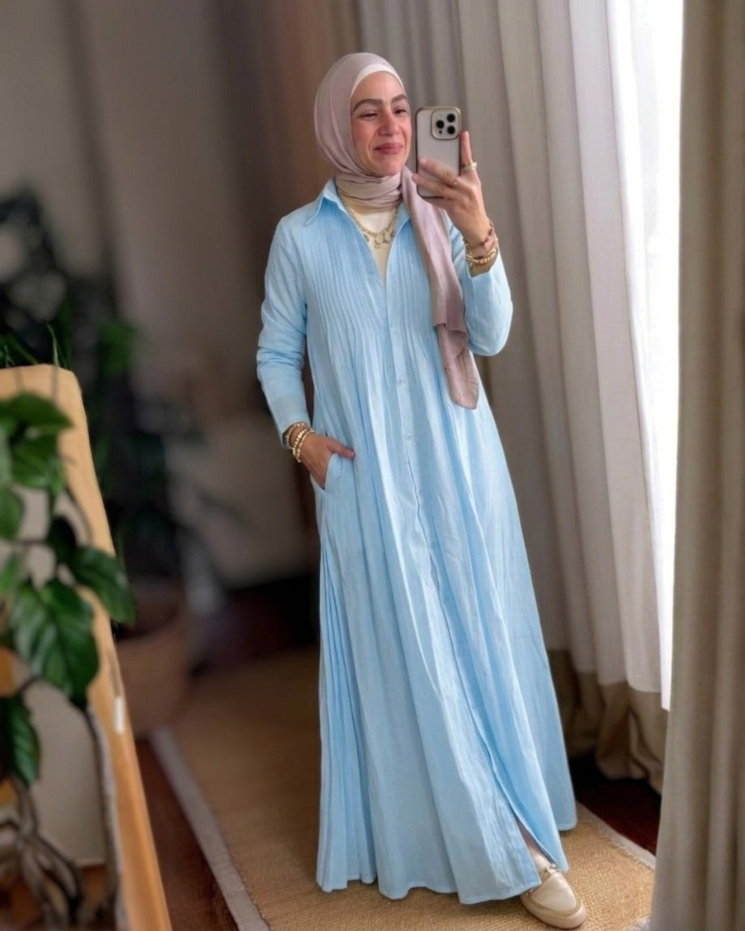 Woman in a light blue dress taking a mirror selfie indoors.