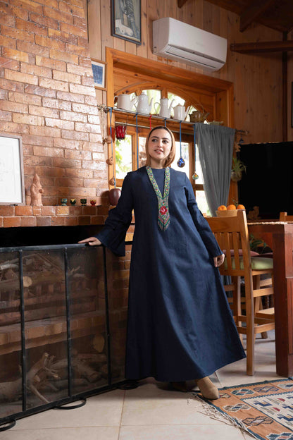 Woman in a blue dress standing in a rustic interior setting with wooden walls and furniture.
